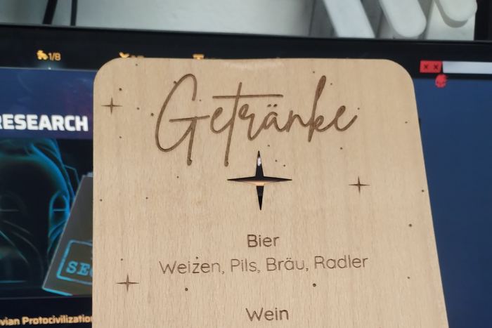 Eine Hand hält eine gravierte Holztafel mit der Überschrift „Getränke“ und einer Liste darunter