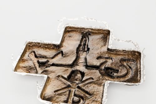 Rekonstruiertes Bronzekreuz von schräg oben: in der Mitte eine Figur mit erhobenen Armen, auf den Querarmen Alpha und Omega, unten ein Christusmonogramm — alles als flaches Relief