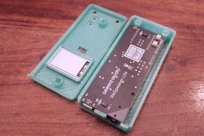 Ein zweiteiliges, durchscheinend grünes 3D-gedrucktes Gehäuse auf einem Holztisch; in der einen Hälfte steckt eine Platine mit Mikrofonen, in der anderen ein kleines Display