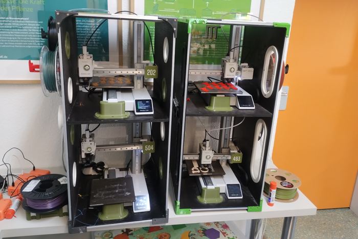 Zwei 3D-Drucker nebeneinander in einem Klassenraum vor grünen Tafeln